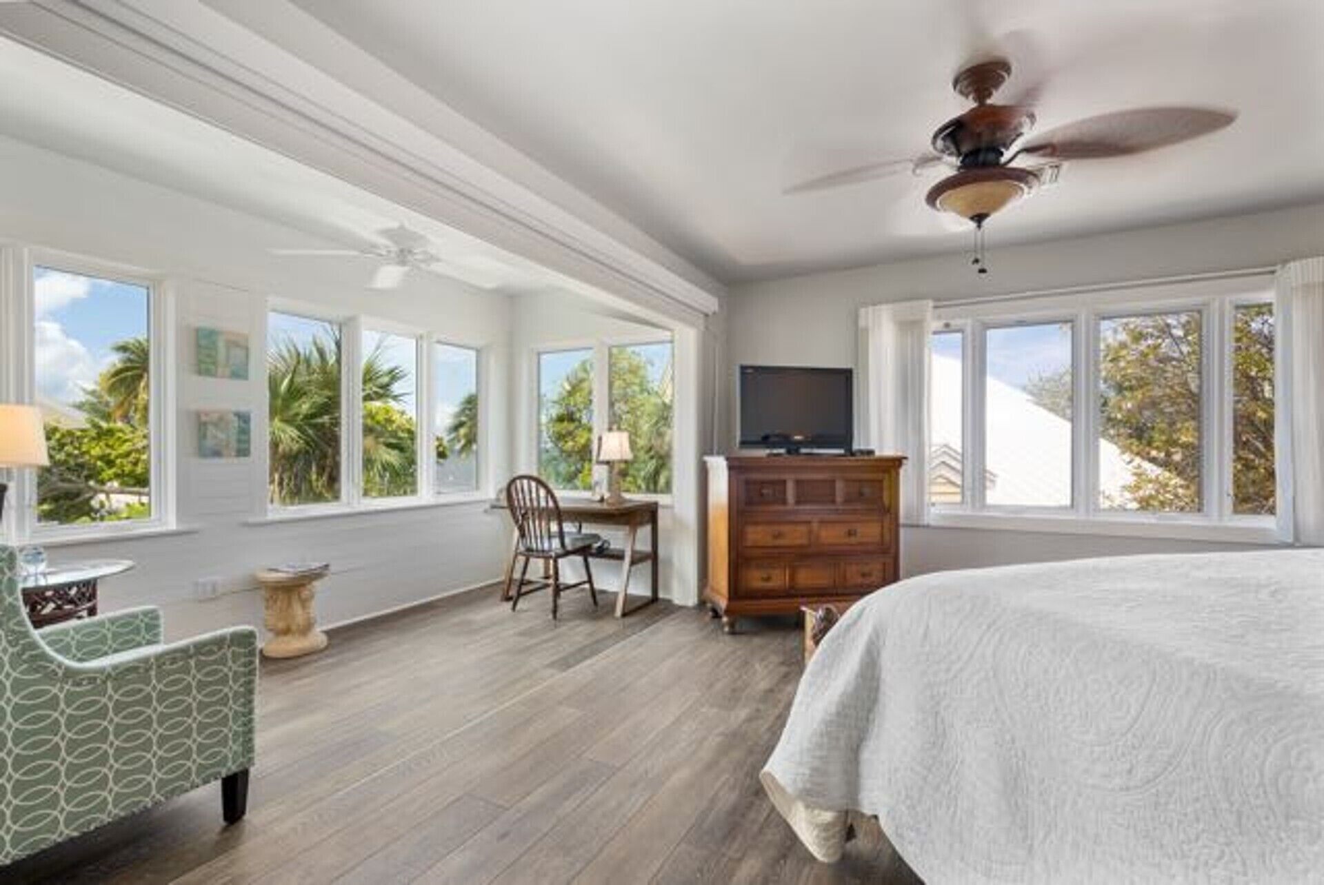 Une chambre spacieuse avec un grand lit, une commode en bois, un téléviseur et un fauteuil.