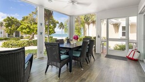 A covered patio with a table and chairs, a ceiling fan, and a view of the ocean.