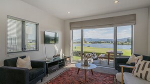 Een moderne woonkamer met een grote televisie, comfortabele zitplaatsen en uitzicht op een meer.