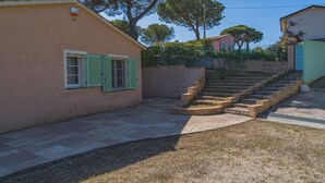 A building with a stone staircase leading to a door, a small garden area with grass and gravel, and a clear sky. - Villa Capo Perla immersed in a magnolia garden a few steps from the sea (Capoliveri)