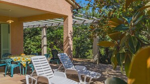 A covered outdoor seating area with lounge chairs and a table, surrounded by greenery. - Villa Capo Perla immersed in a magnolia garden a few steps from the sea (Capoliveri)