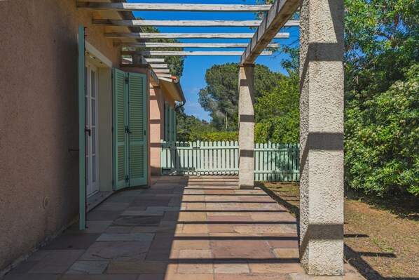 A covered outdoor area with stone flooring, a wooden pergola, and a white fence.