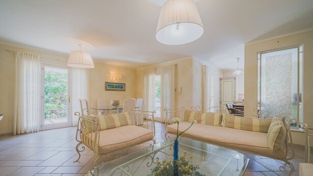 A spacious living room with a glass coffee table, a sofa set, and a dining area. - Villa Capo Perla immersed in a magnolia garden a few steps from the sea (Capoliveri)