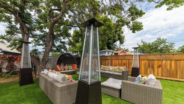 Un jardin avec une pelouse artificielle, des meubles en osier et deux grands radiateurs noirs.