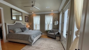 Quarto com uma cama grande, uma cadeira, um ventilador de teto e janela com cortinas.
