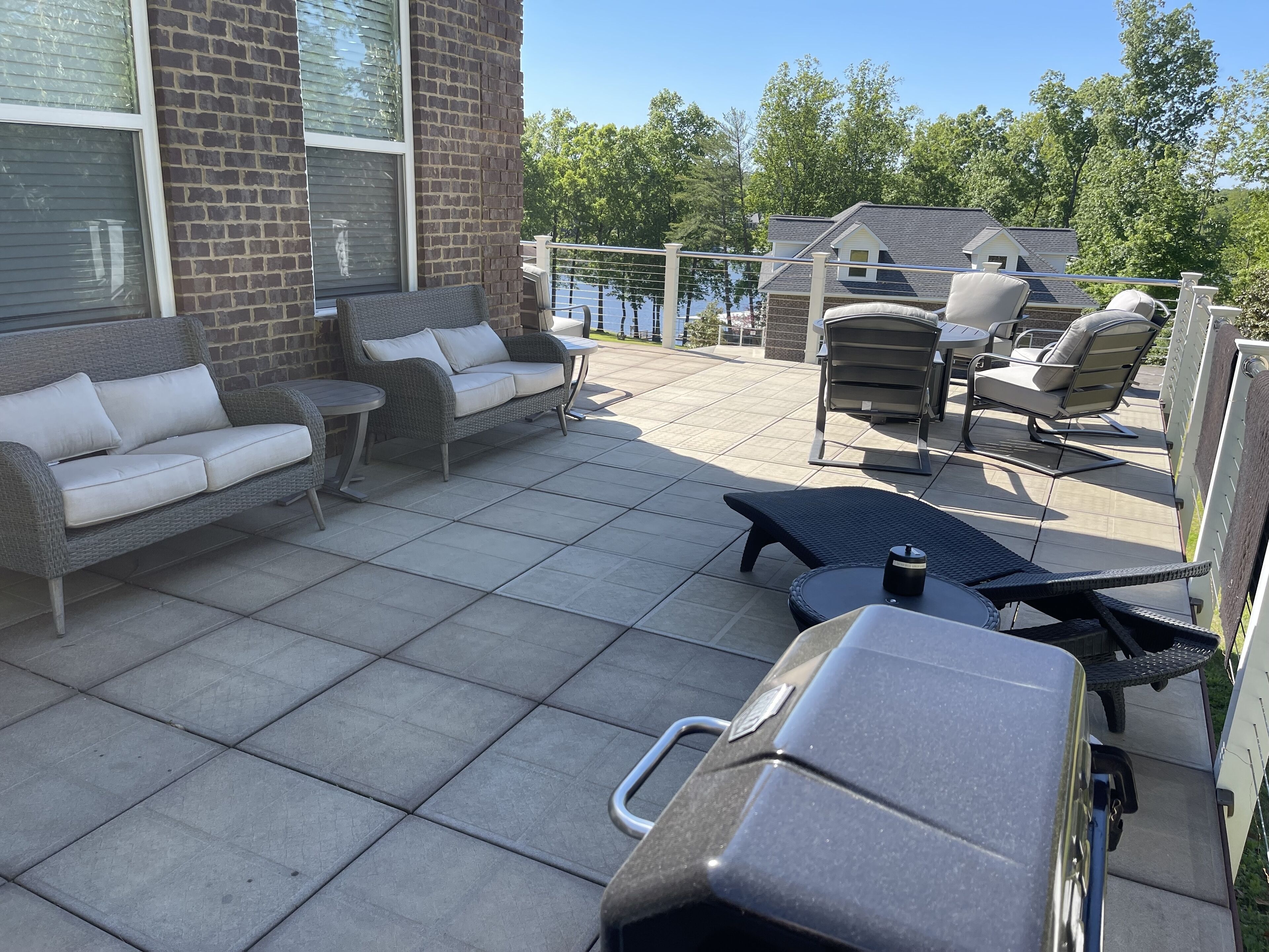 Een terras met een grijze wickerbank, een kleine ronde tafel en een zwarte lounge stoel.