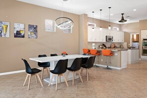 A modern kitchen with white cabinets, a central island with orange bar stools, and a dining area with a white table and black chairs. - Golf Course Home w/ Private Pool, Spa, Casita, Firepit & Covered Patio Dining (Palm Desert)