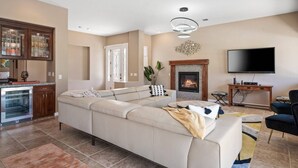 Ein modernes Wohnzimmer mit Ecksofa, Kamin, Flachbildfernseher und Küchenzeile mit Kühlschrank und Schränken.