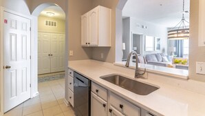 A modern kitchen with white cabinetry, a stainless steel sink, and a large mirror above the counter. - Disney Escape | Renovated Windsor Hills Condo w/ Balcony & Themed Bedrooms (Kissimmee)