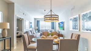 A modern dining area with a round table, chairs, and a hanging light fixture. - Disney Escape | Renovated Windsor Hills Condo w/ Balcony & Themed Bedrooms (Kissimmee)