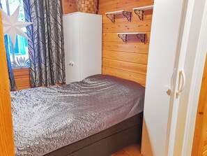 A bedroom with a bed, wardrobe, and shelves against a wooden wall. - Piilola nr 1 by Interhome (Kuusamo)