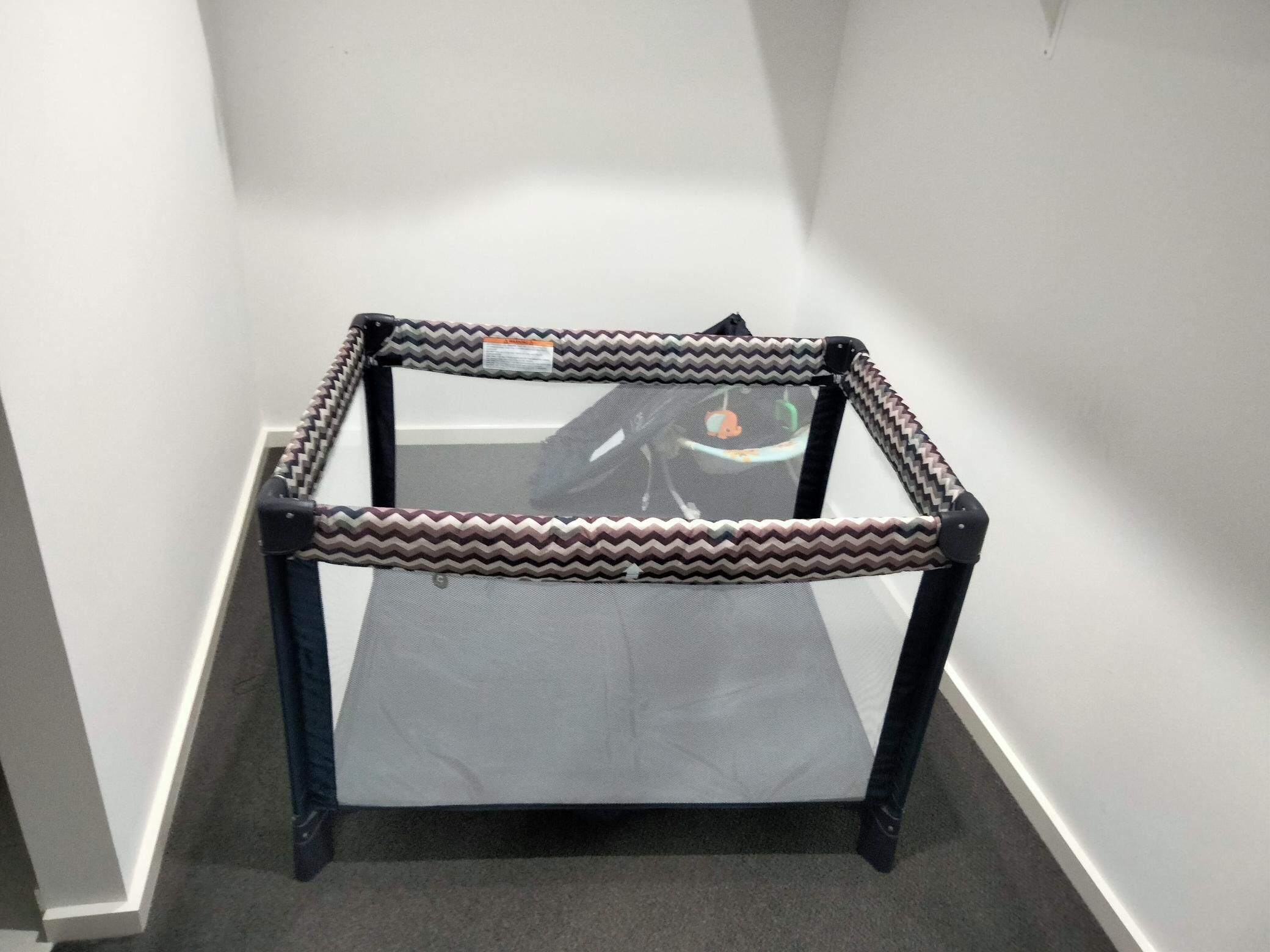 A corner table with a zigzag patterned frame and a mesh surface, placed in a hallway with white walls and carpet flooring.