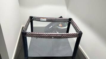 A corner table with a zigzag patterned frame and a mesh surface, placed in a hallway with white walls and carpet flooring.