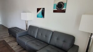 Una sala de estar moderna con un sofá gris, una lámpara de pie y dos obras de arte colgadas en la pared.