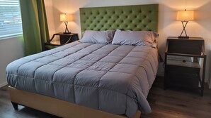 Una cama bien hecha con cabecera verde, dos mesitas de noche con lámparas y arte abstracto en la pared.