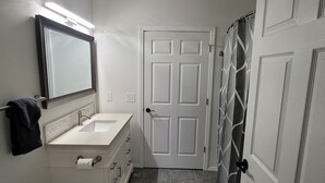 Baño con lavamanos, espejo y puerta blancos.