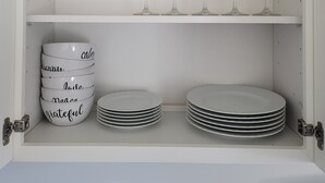 Un armario blanco con estantes que contienen copas de vino, cuencos con palabras y platos apilados.