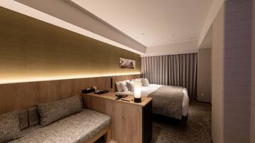 Une chambre d’hôtel moderne avec un mur d’accent en bois, un canapé, un lit avec une couverture grise et une table de chevet avec une lampe.
