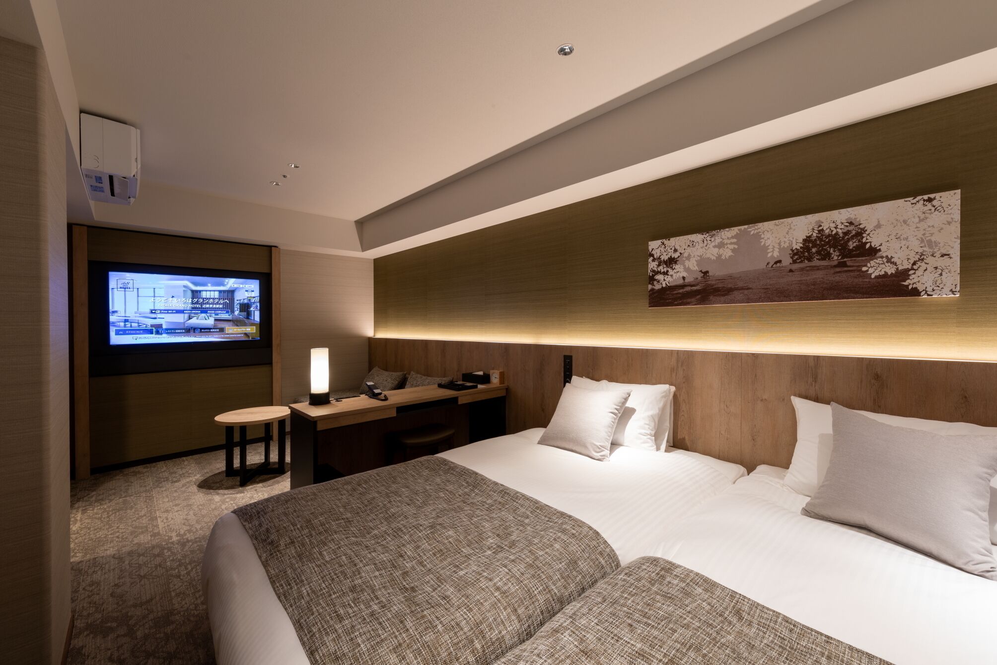 A hotel room with a large bed, a desk with a chair, a television, and a wall-mounted artwork.