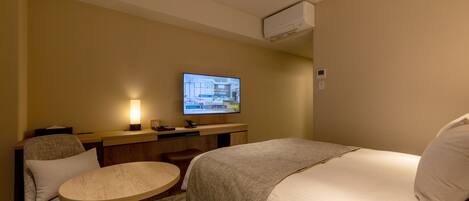 A hotel room with a bed, a desk, a chair, a television, and an air conditioning unit.