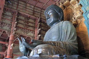 Una estatua grande de Buda en un templo con arquitectura de madera tradicional y ornamentos dorados intrincados.