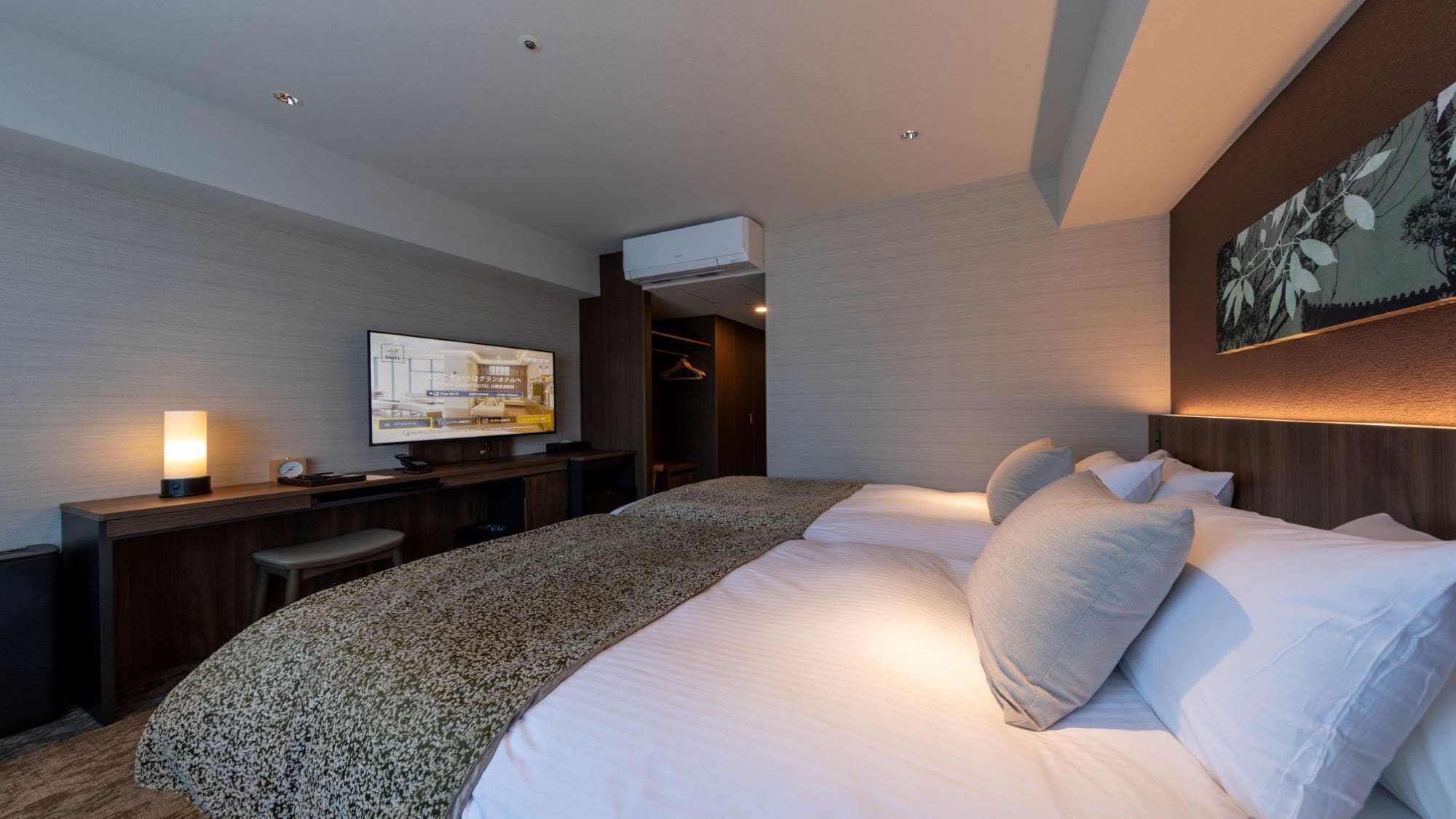 A hotel room with a large bed, a desk with a computer, a TV, and a wardrobe.