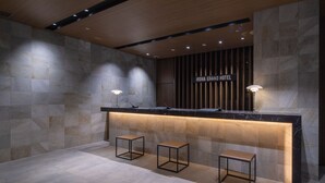 A reception area with a stone wall, a wooden ceiling, and a sign that reads "IROHA GRAND HOTEL". There are three stools and two table lamps. - IROHA GRAND HOTEL KINTETSUNARAEKIMAE (Nara)