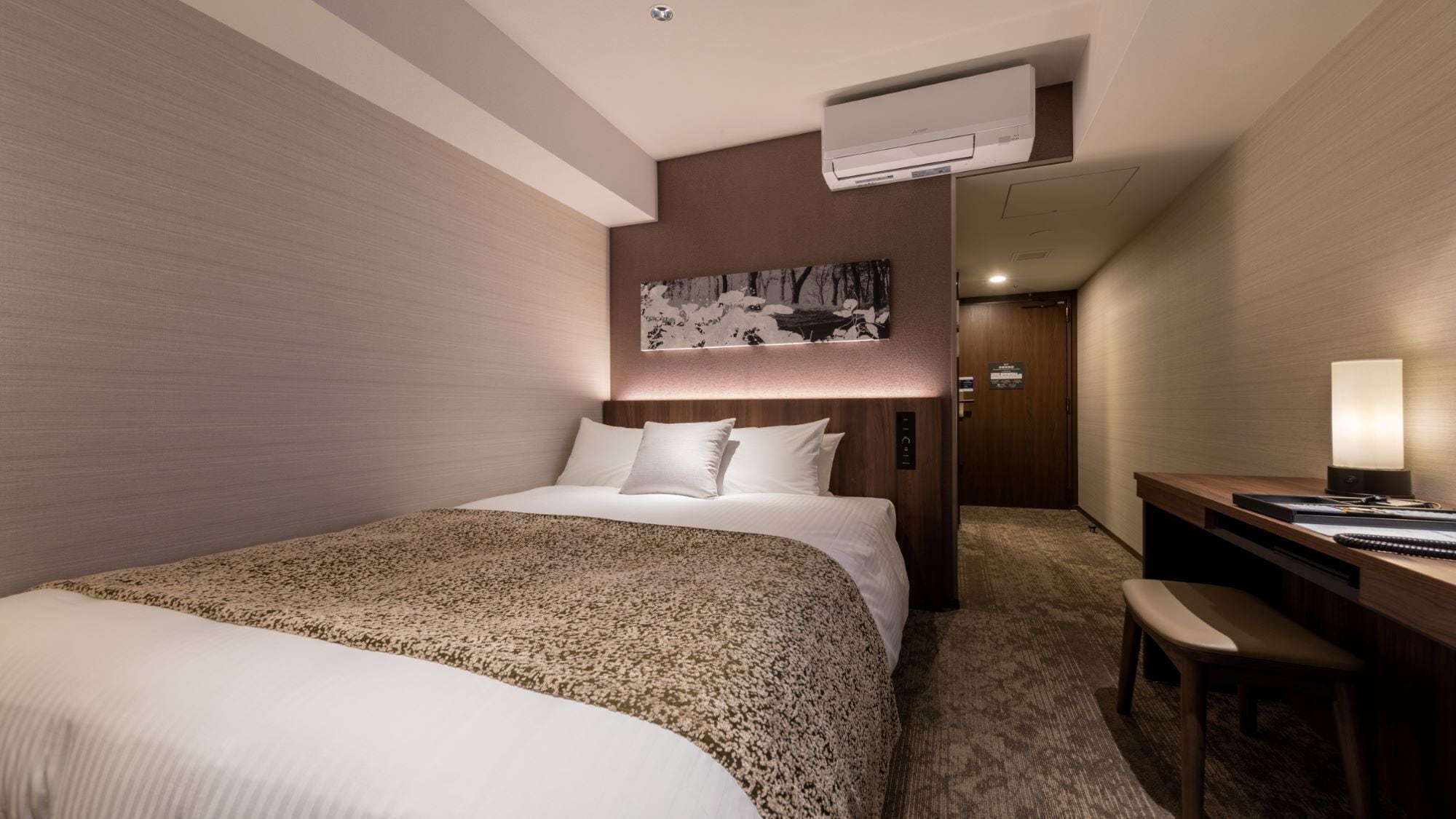 Habitació d'hotel amb un llit gran, un escriptori amb cadira i aire condicionat fixat a la paret.