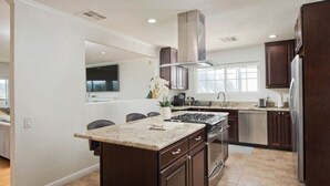 A modern kitchen with dark wood cabinets, a granite countertop, stainless steel appliances, and a large island with seating. - calabasas Home With stunning Views, Pool, and Jacuzzi  (Calabasas)