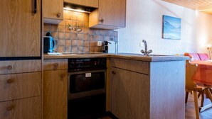 A compact kitchen with wooden cabinets, a built-in oven, a coffee maker, and a tiled backsplash. - Südlenz 32 3. OG Süd by Interhome (Riederalp)