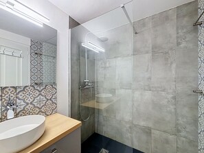 A modern bathroom with a large mirror, a white sink, a shower with a glass door, and patterned tiles.