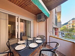 An outdoor balcony with a table set for four, wicker chairs, and a view of the street and buildings.