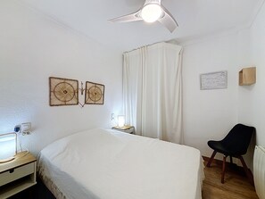 A bedroom with a bed, a chair, a bedside table with a lamp, a ceiling fan, and two wall-mounted decorative items.