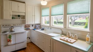A kitchen with white cabinets, a stove, a sink, and a window with blinds. - Homeplace 1936 | Walk to Downtown West Jefferson | Historic High Country Stay (West Jefferson)