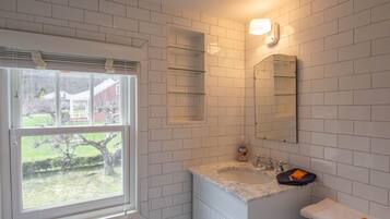 A bathroom with white tiled walls, a window, a sink, a mirror, and a towel on the counter.