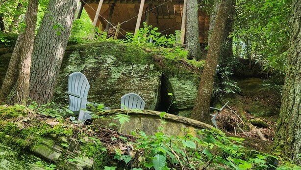 A wooden cabin with a balcony, surrounded by trees and rocks.