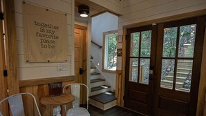 A wooden interior with a staircase, a small table with chairs, and a door leading outside.