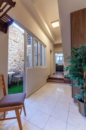 A hallway with a wooden chair, a potted plant, a stone wall, and a view into a kitchen area.