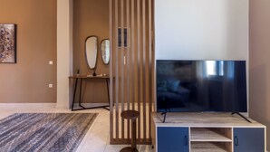 Una sala de estar moderna con un televisor de pantalla plana grande, un separador de madera y una pequeña mesa redonda con una planta.