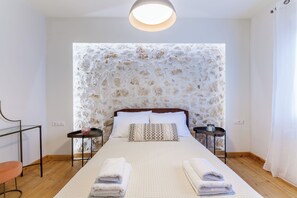 A neatly made bed with white linens, two bedside tables with lamps, a wooden floor, and a stone-patterned wall.