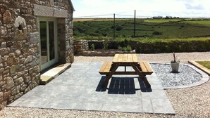 A stone building with a wooden picnic table and a potted plant. - Coastal Barn Conversion, overlooking the stunning Cot valley. (Saint Just)