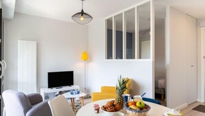 En moderne stue med et fladskærms-tv, et spisebord dækket til morgenmad, og et stort vindue med udsigt.