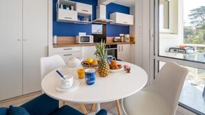Et moderne køkken med hvide skabe, en mikroovn og en kaffemaskine. Der er et spisebord med hvid dug, en skål med frugt og en ananas.