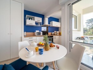 A modern kitchen with white cabinets, a microwave, and a coffee maker. There is a dining table with a white tablecloth, a bowl of fruit, and a pineapple.