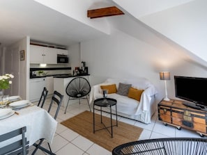 Un espace de vie compact comprenant un coin cuisine, un coin repas et un espace détente avec un canapé et un téléviseur.