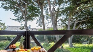 Un espace de restauration en plein air avec une table dressée pour le petit-déjeuner, comprenant des fruits, du pain et du jus, donnant sur un jardin luxuriant et des arbres.