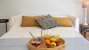 Un lit bien fait, avec un plateau de petit-déjeuner comprenant des fruits, du jus et une bouteille de lait.