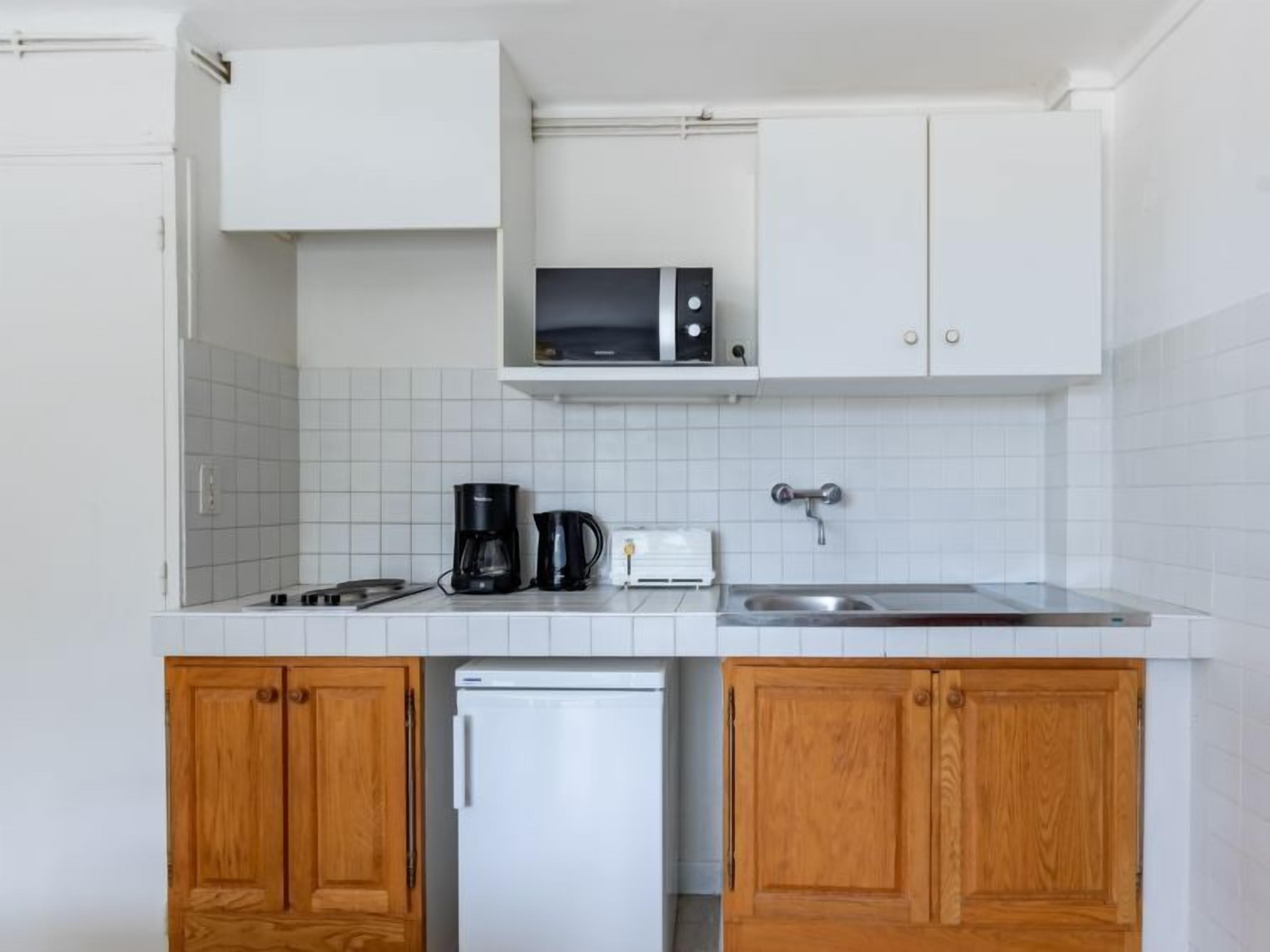 A compact kitchen with white cabinets, a microwave, a coffee maker, and a toaster.