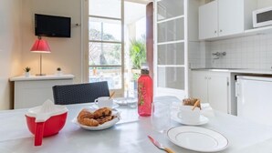 A modern kitchen with white cabinets, a flat-screen TV, and a dining table set with croissants, a red juicer, and a pink water bottle. - Super Plage by Interhome (Saint Cyr sur mer Les Lecques)
