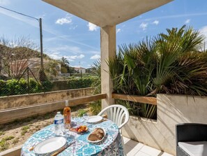 A covered outdoor dining area with a table set for two, featuring a patterned tablecloth, plates, cutlery, a bottle, and a loaf of bread. - Super Plage by Interhome (Saint Cyr sur mer Les Lecques)